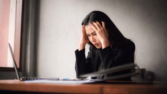 Presenteeism at work - woman sat at a desk with her head in her hands and looking pensive