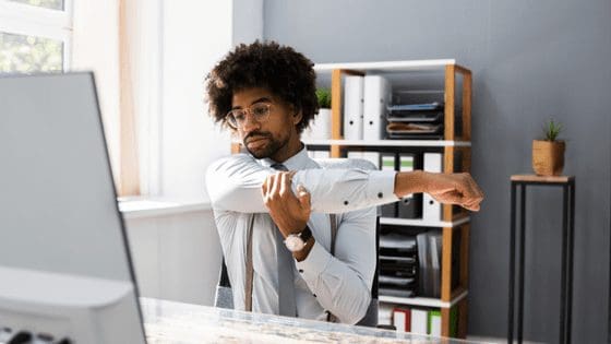 Man-stretching-while-working-at-his-desk-no-work-life-balance.png