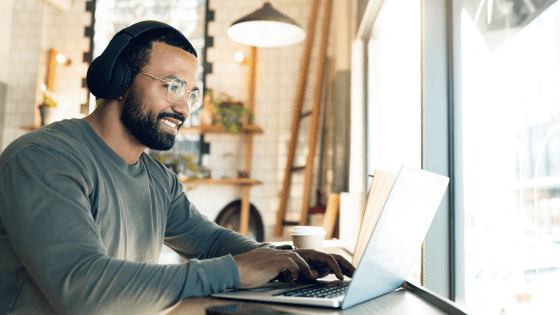Man sat as a desk in front of a laptop wearing headphones